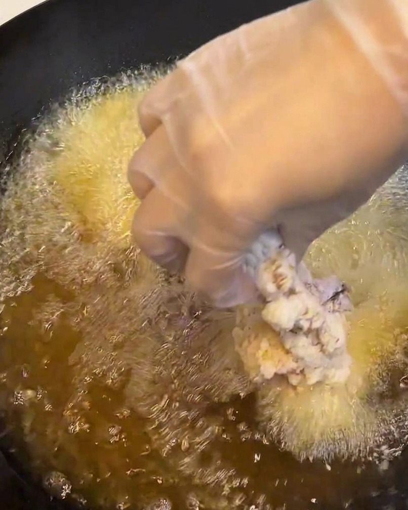 Un filete de pollo rebozado bajándose a una sartén con aceite caliente.