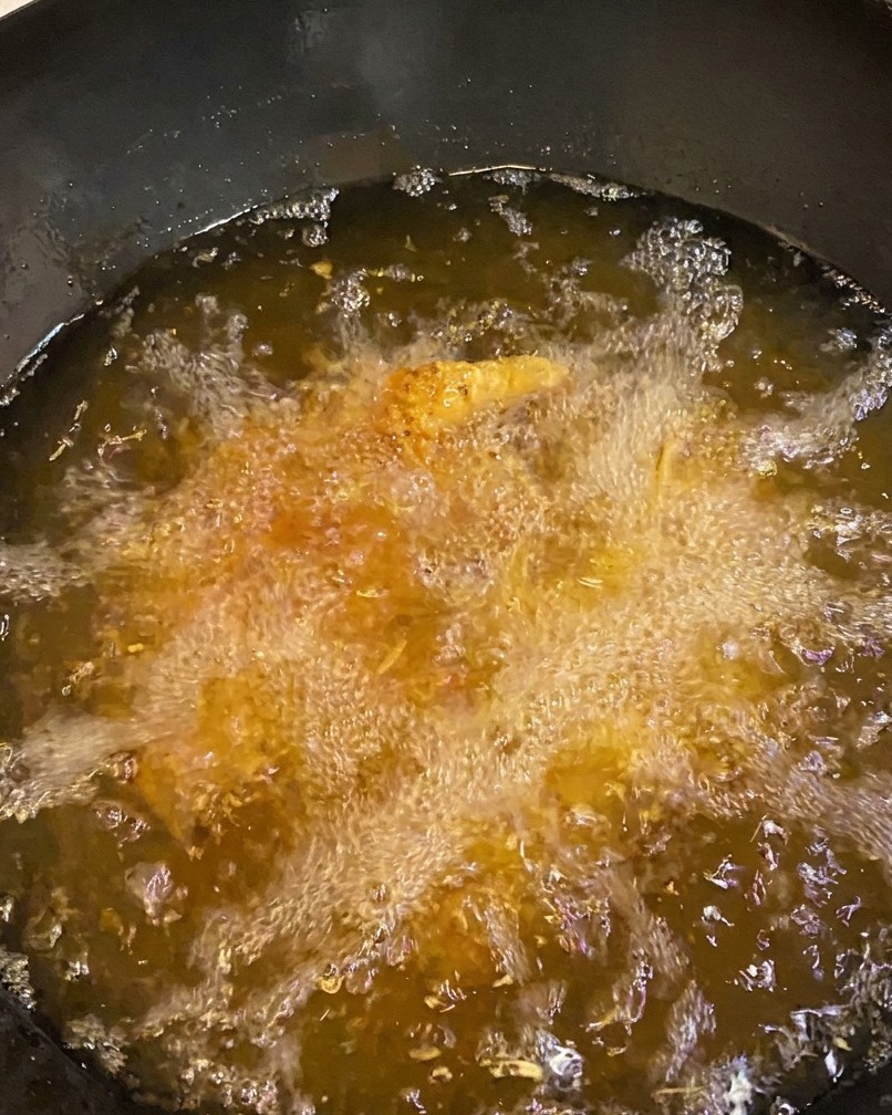 Filetes de pollo friéndose en aceite, mostrando una corteza dorada.
