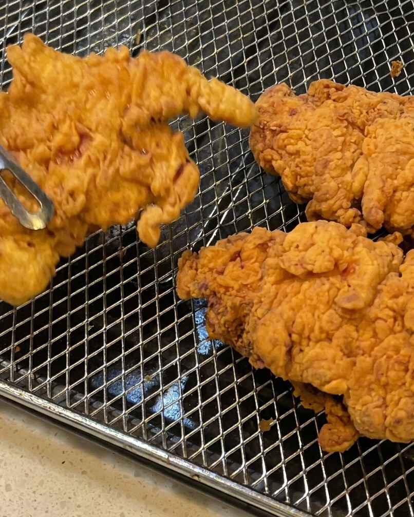 Pollo frito siendo retirado del aceite con pinzas.