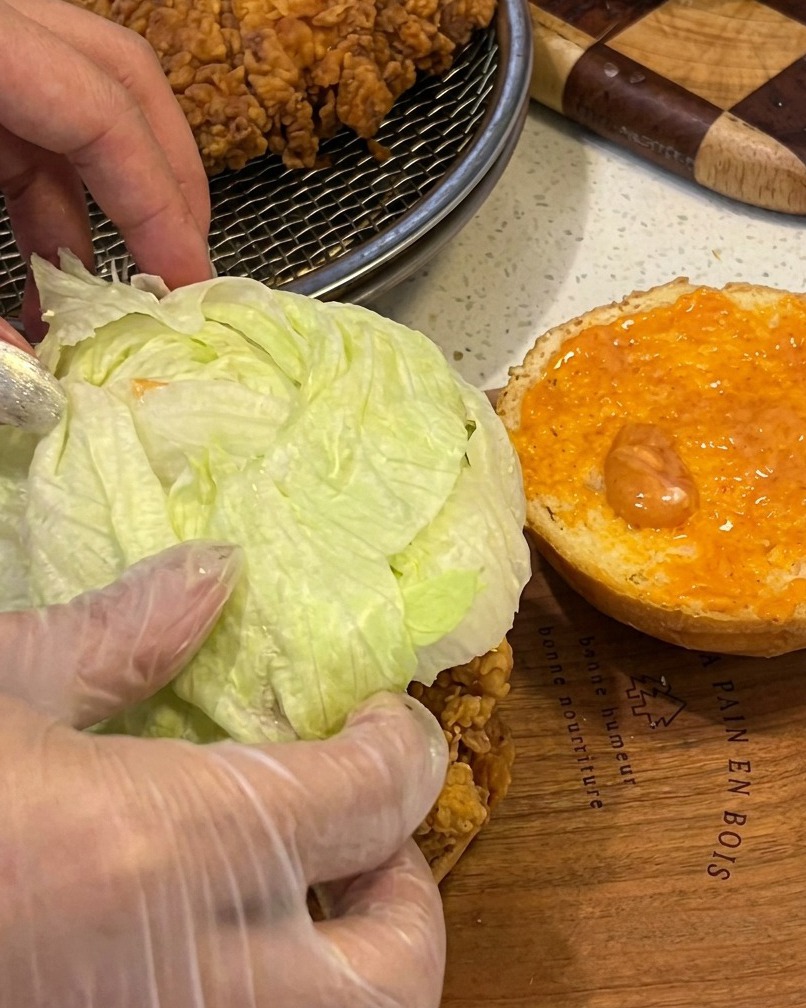 Montaje de la hamburguesa con pollo, lechuga y salsa sobre pan tostado.
