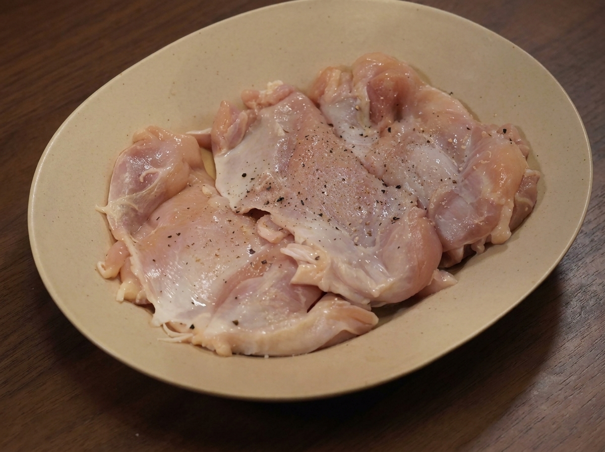 Muslos de pollo crudos en un plato espolvoreados con varias especias secas.