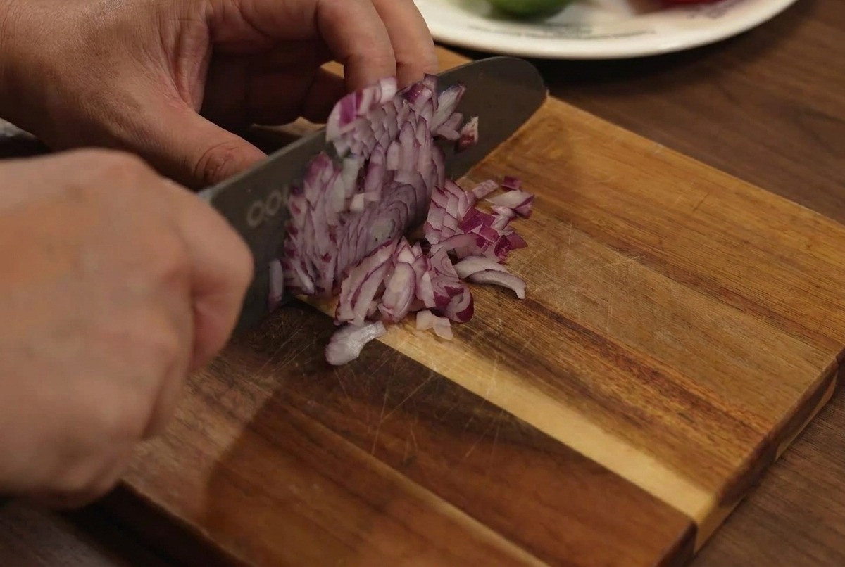 Cebolla roja siendo picada finamente sobre una tabla de cortar de madera con un cuchillo.