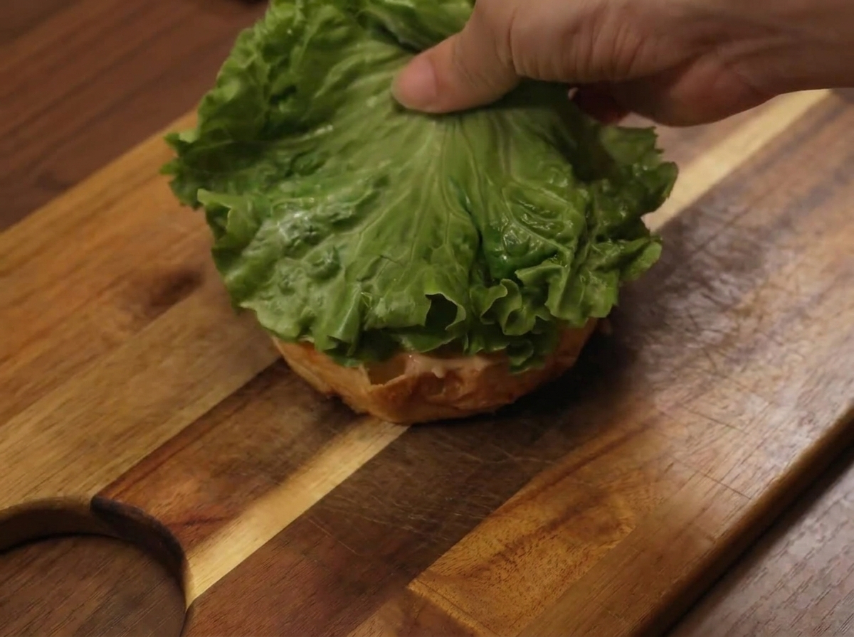 Una hoja de lechuga colocada sobre el pan inferior durante el montaje de la hamburguesa.