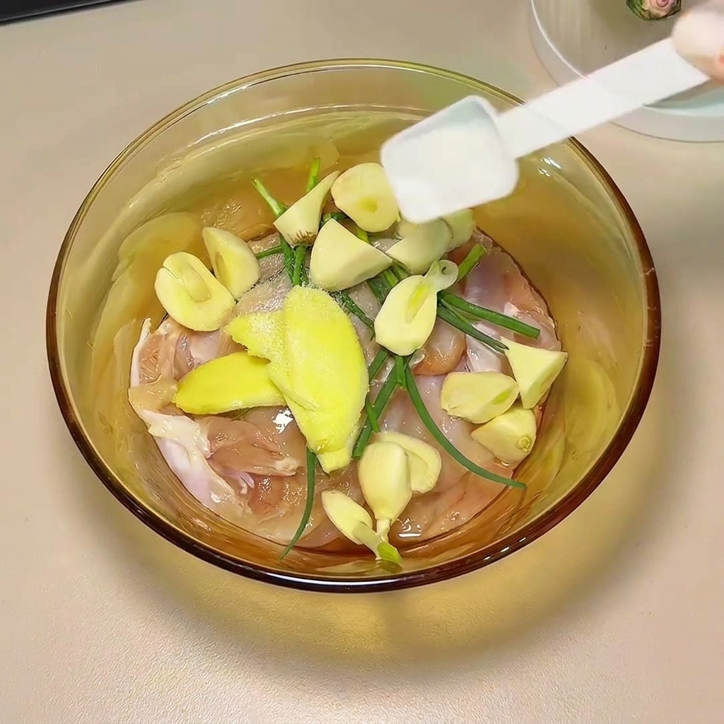 Salsa de soja y especias vertiéndose sobre los muslos de pollo y los aromáticos en un cuenco de cristal.