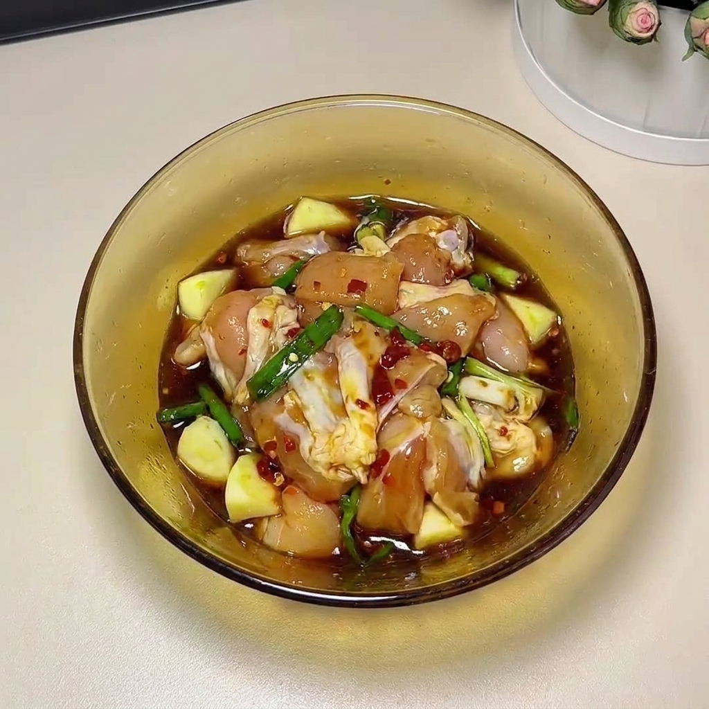 Muslos de pollo crudos siendo masajeados a mano con los ingredientes del marinado en un cuenco de cristal.
