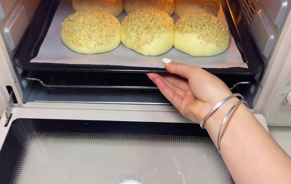 Una bandeja de bolas de masa reposadas y cubiertas de sésamo siendo introducidas en un horno precalentado.