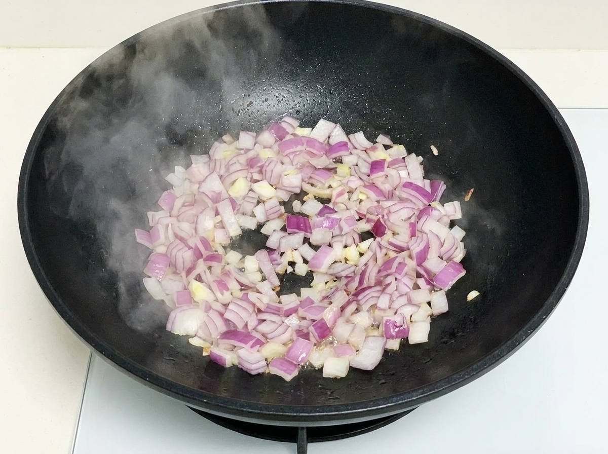 Cebollas moradas picadas salteándose en un wok negro caliente con vapor visible.