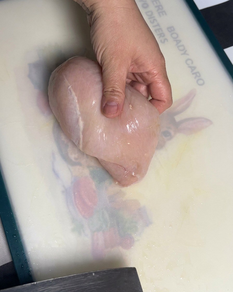 Pechuga de pollo cruda siendo cortada en trozos uniformes sobre una tabla de cortar.