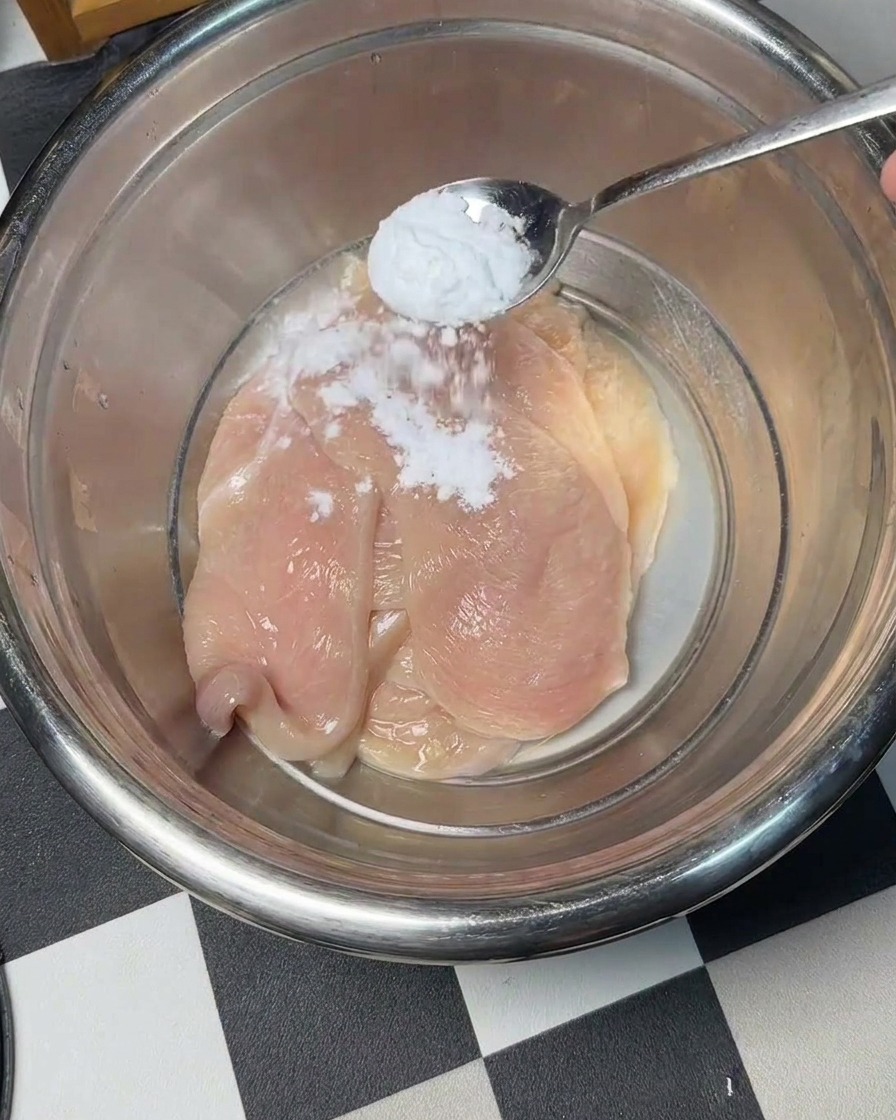 Bicarbonato de sodio siendo espolvoreado sobre trozos de pollo crudo en un bol.