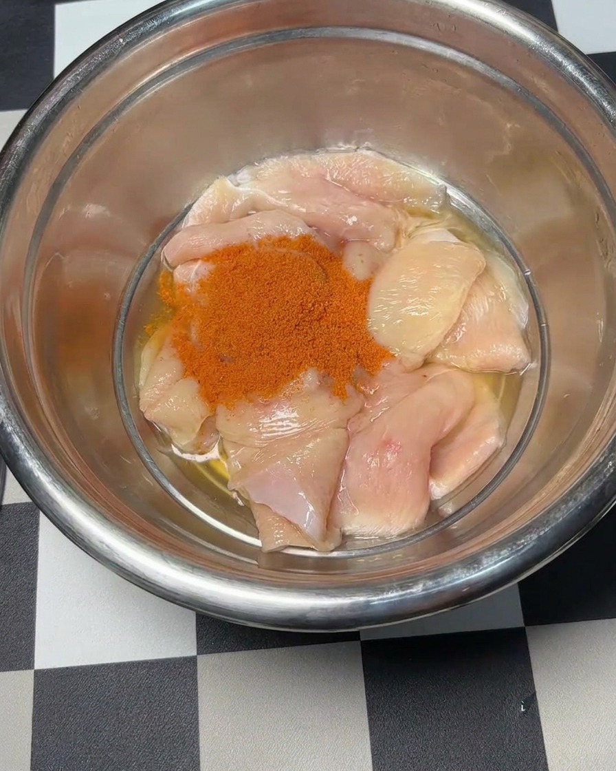 Polvo de marinado Orleans rojo siendo vertido sobre los trozos de pollo crudo.