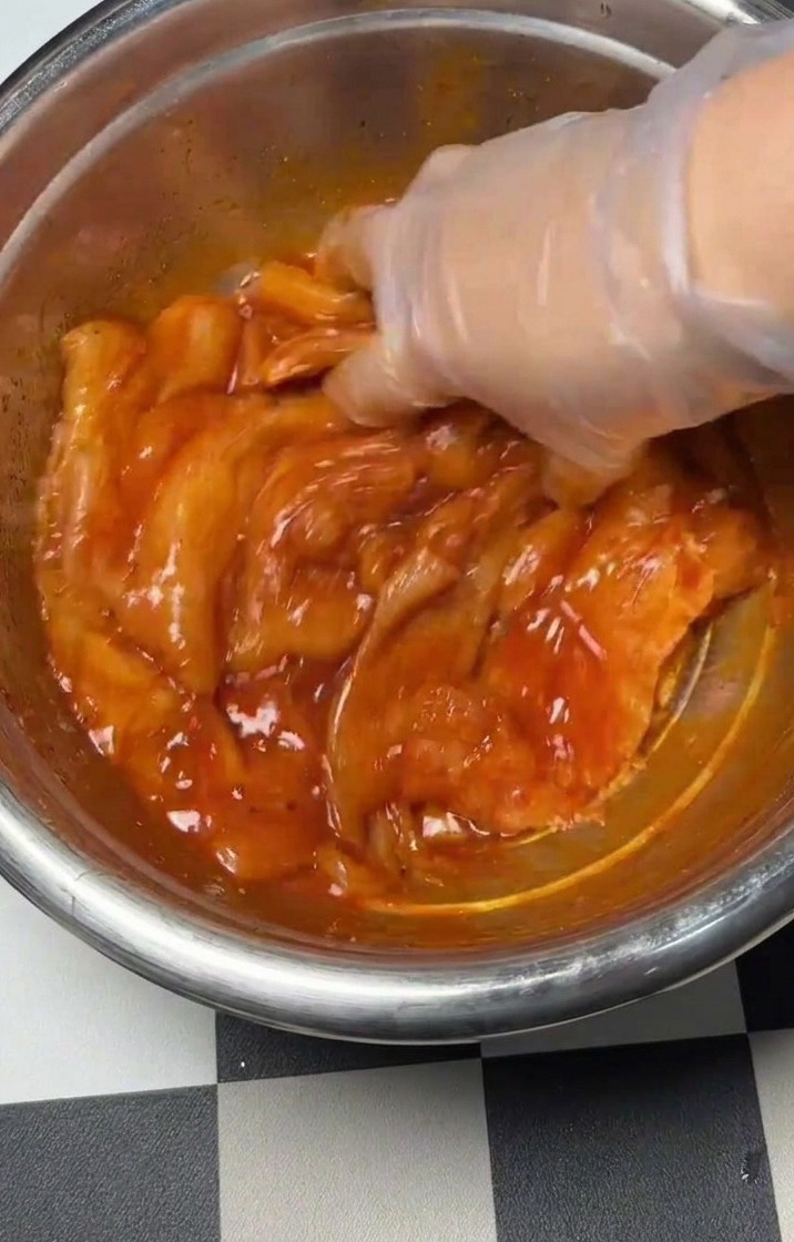 Mezclando a mano el pollo sazonado y el marinado en un bol de metal.
