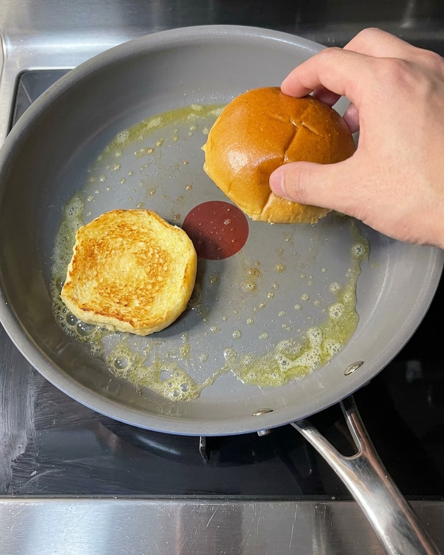 Panes de hamburguesa en una sartén con mantequilla derretida burbujeante, en proceso de tostado.