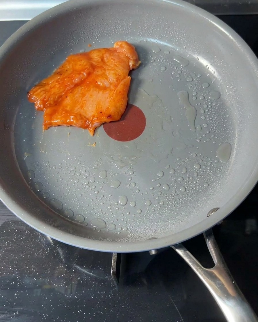 Hamburguesas de pollo sazonado crudo colocadas en una sartén caliente con una capa ligera de aceite.