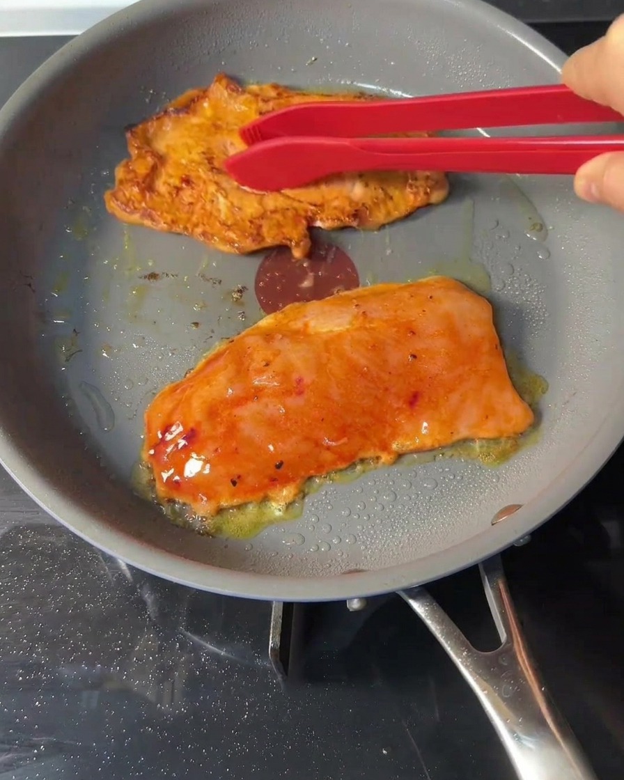Pinzas de silicona rojas volteando piezas de pollo dorándose dentro de una sartén.