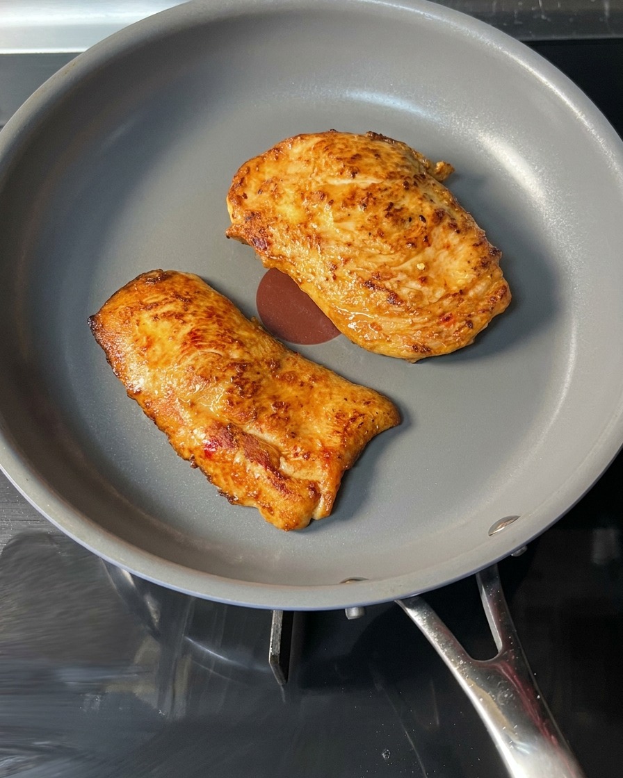 Una pieza de pollo dorada siendo retirada de la sartén con pinzas rojas.