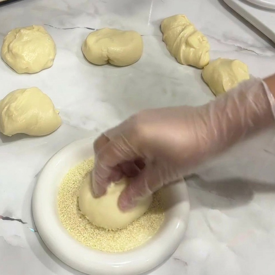 Mano colocando una bola de masa en un plato con semillas de sésamo.