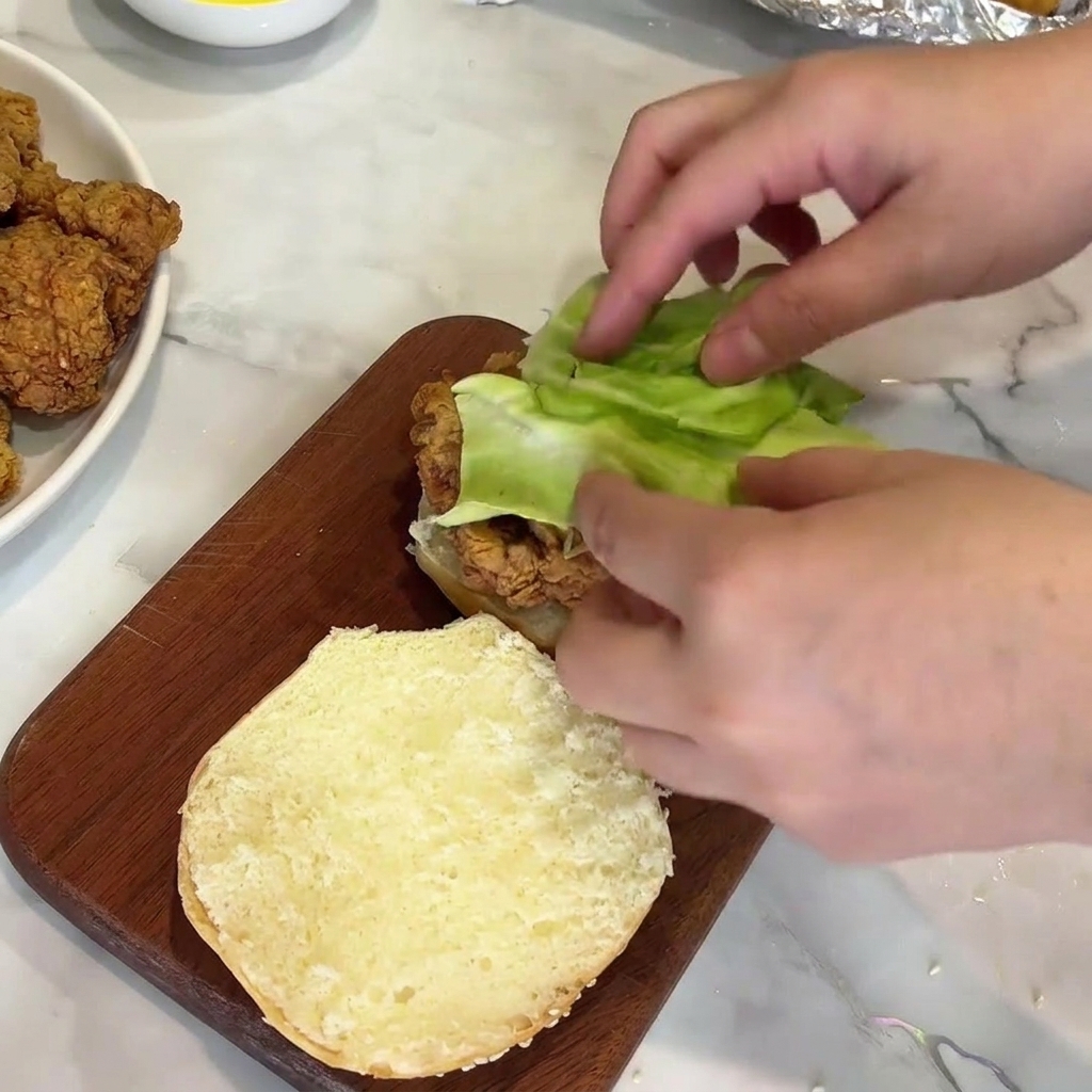 Colocando lechuga sobre una hamburguesa de pollo.
