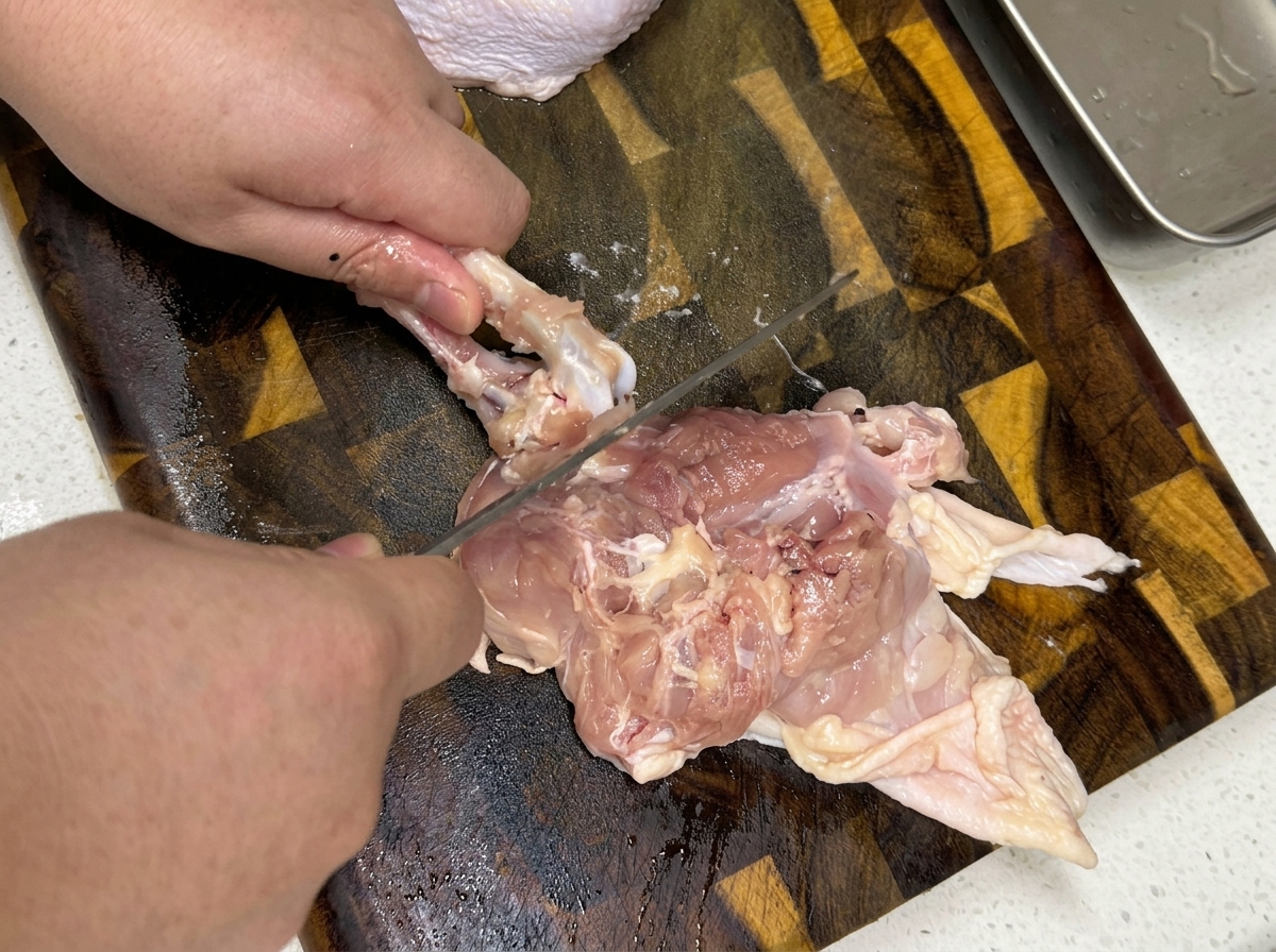 Primer plano de manos deshuesando un muslo de pollo crudo sobre una tabla de cortar de madera.