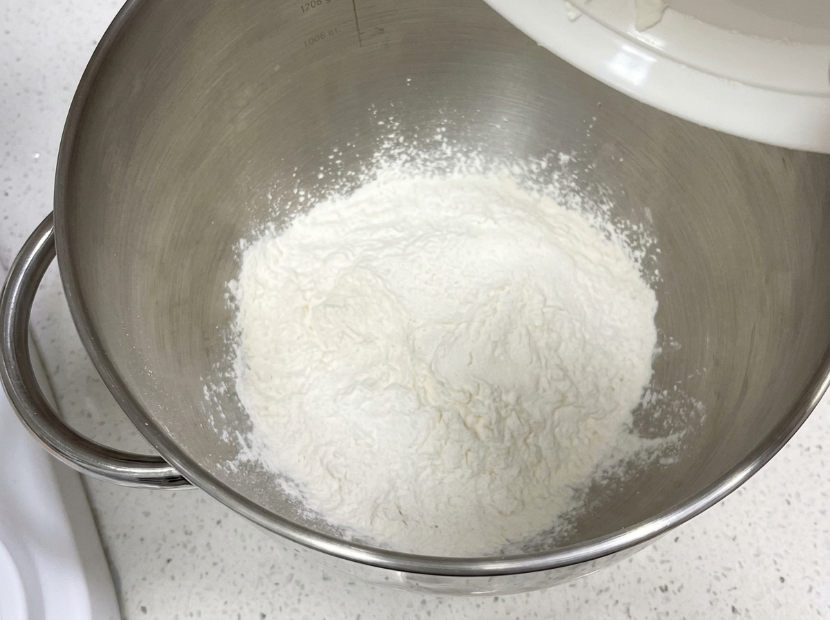 Harina seca e ingredientes en el cuenco de una batidora de pie.