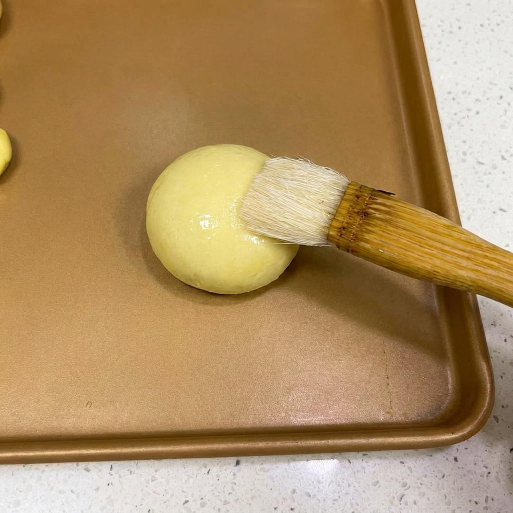 Una brocha de repostería aplicando una fina capa de agua sobre la parte superior de una bola de masa.