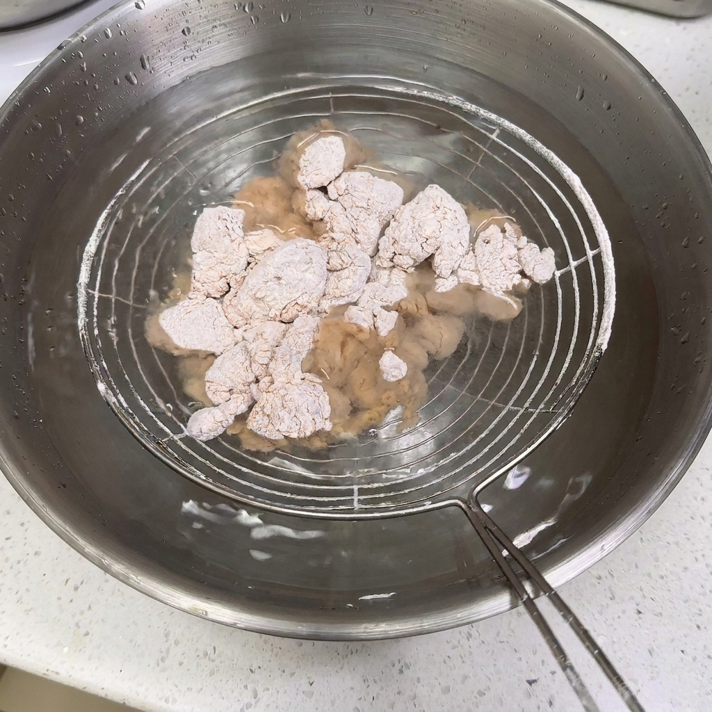 Trozos de pollo enharinados sumergidos en un cuenco de acero inoxidable con agua.