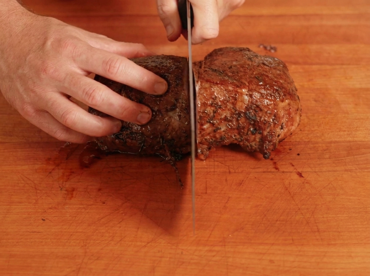 Un roast beef cocinado siendo cortado por la mitad en una tabla de cortar.