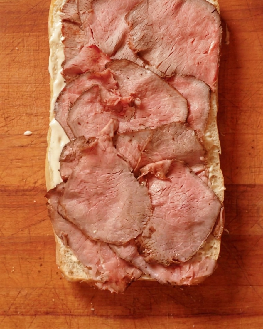 Roast beef cocinado y cortado finamente dispuesto sobre una capa de salsa en el pan.