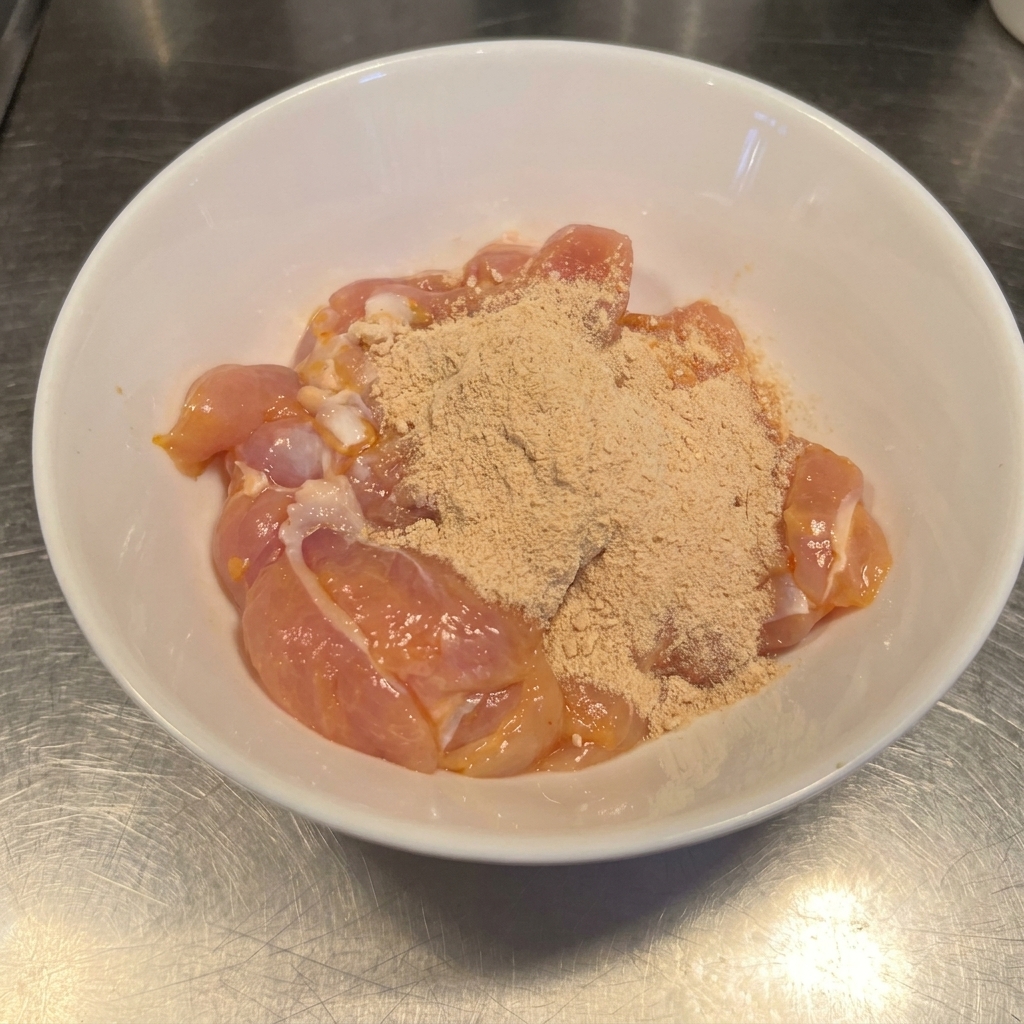 Muslos de pollo crudos en un bol cubiertos con una mezcla de chile rojo en polvo y ajo.