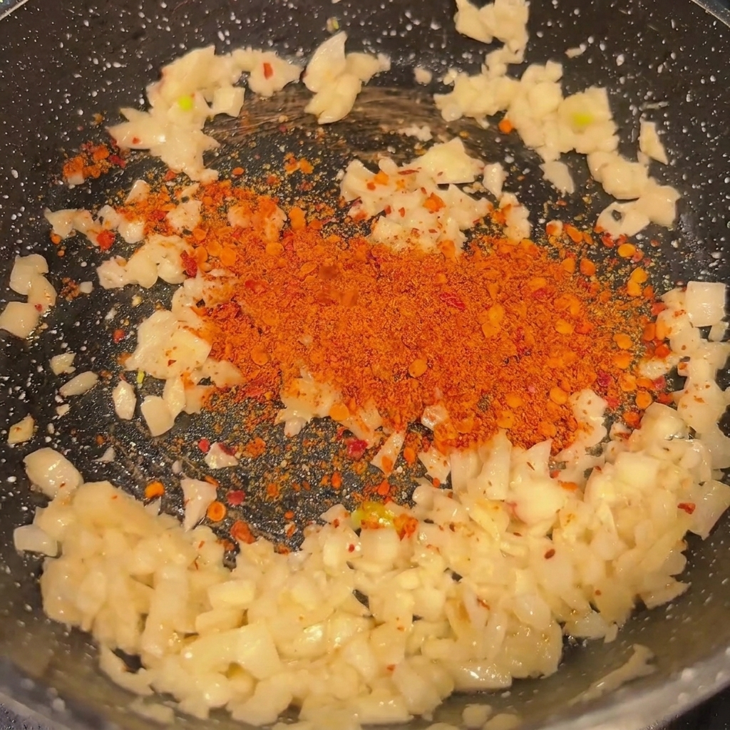 Ajo picado y chile en polvo sofriéndose en una sartén negra caliente.