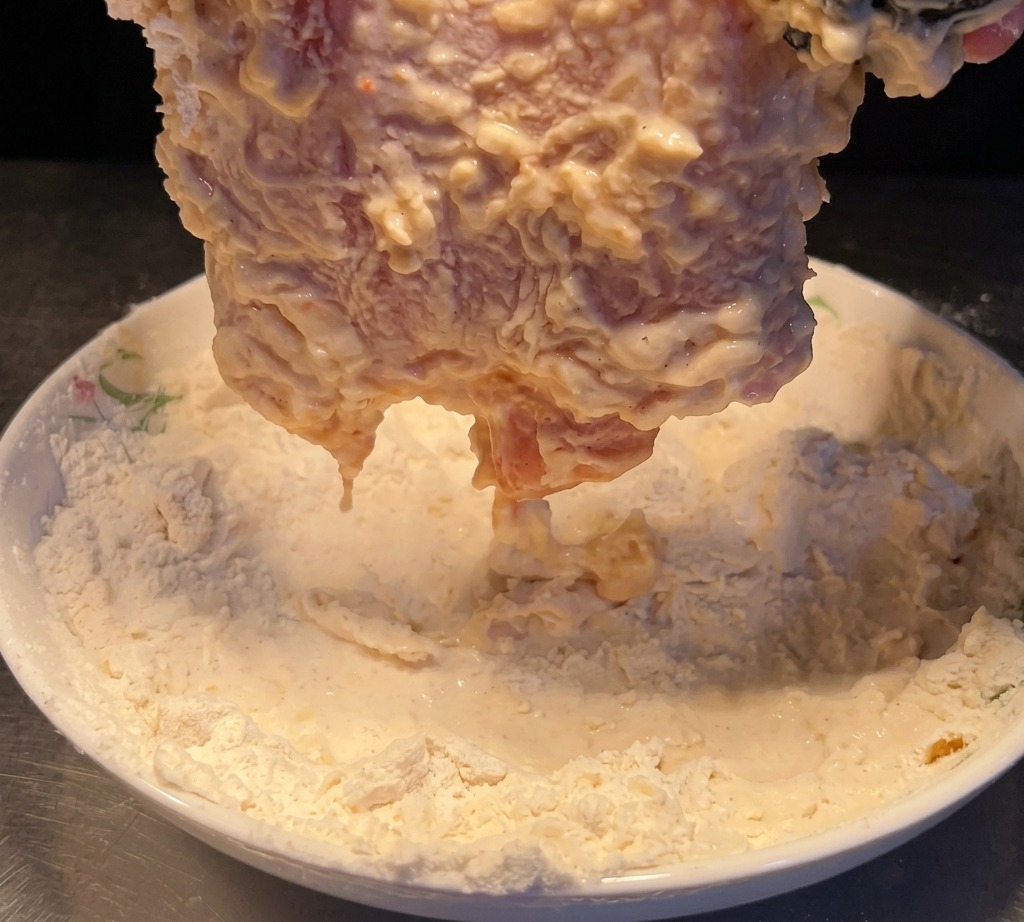 El pollo humedecido siendo presionado nuevamente en la harina seca para crear una segunda capa.