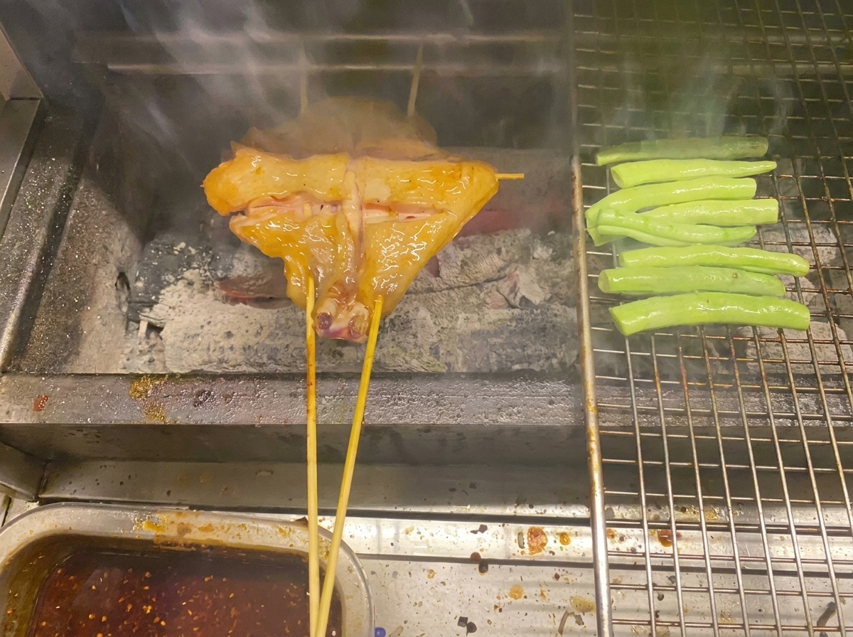 Brochetas de pollo y judías verdes cocinándose sobre carbón en una parrilla de metal.