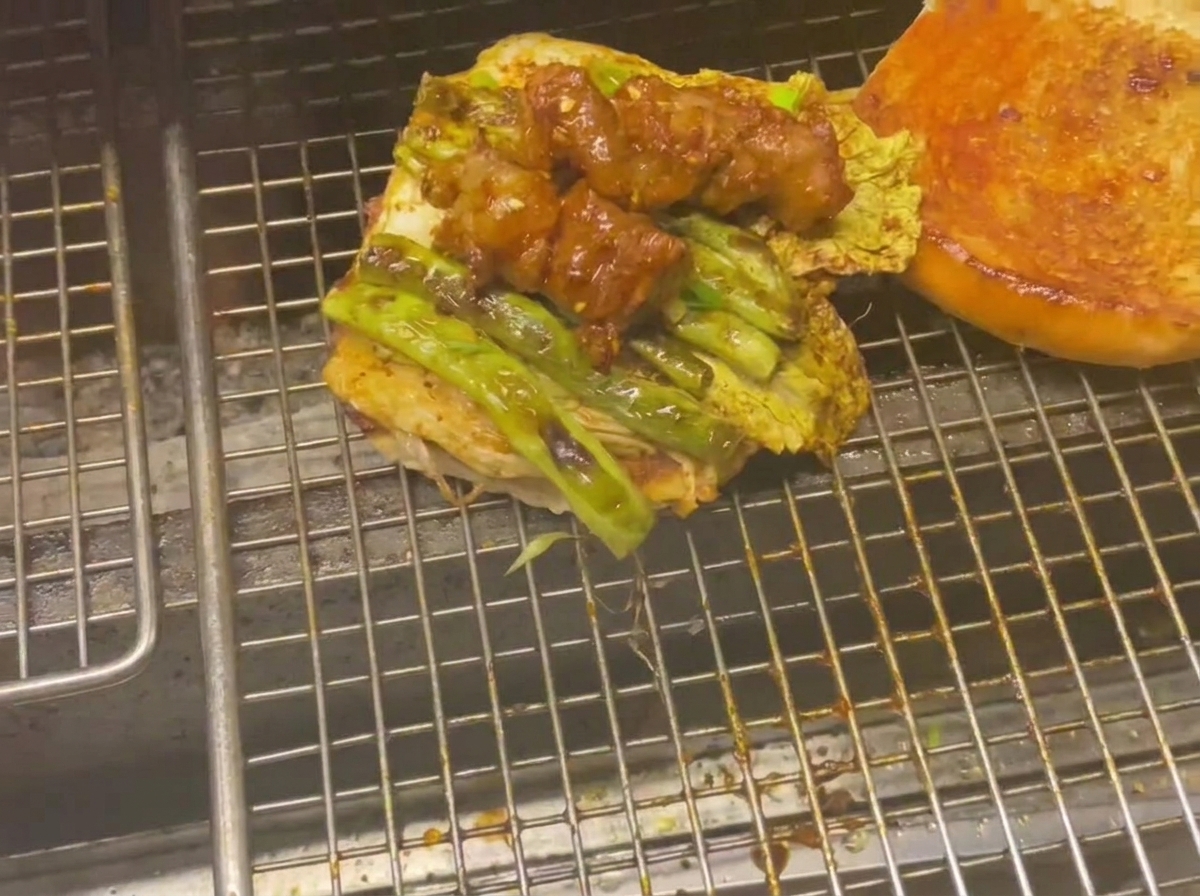 Mitad inferior de un pan de hamburguesa cubierto con vegetales y brochetas de carne glaseadas en la parrilla.