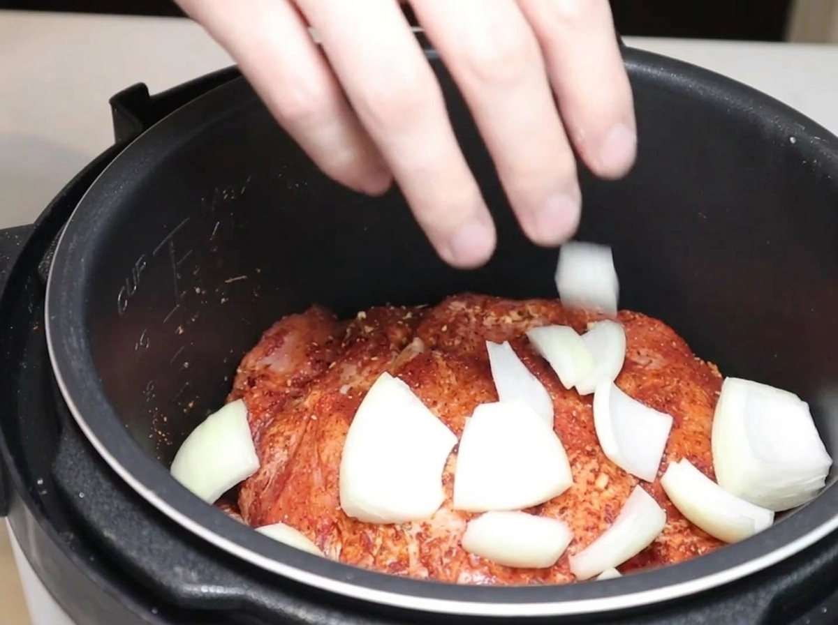 Gajos de cebolla y chiles secos siendo añadidos a la olla con el cerdo.