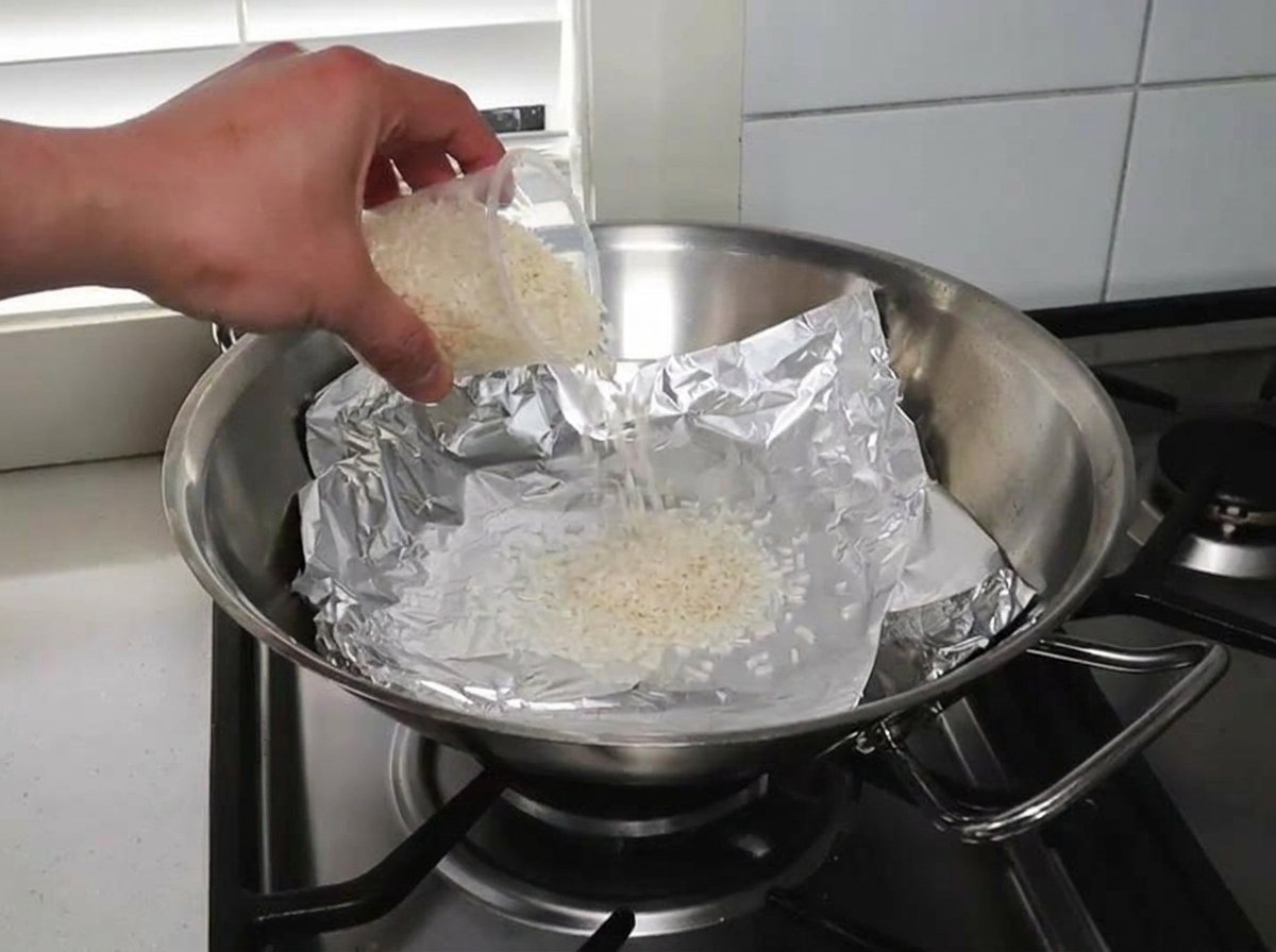 Arroz crudo y astillas de madera esparcidos sobre un wok forrado con papel aluminio.
