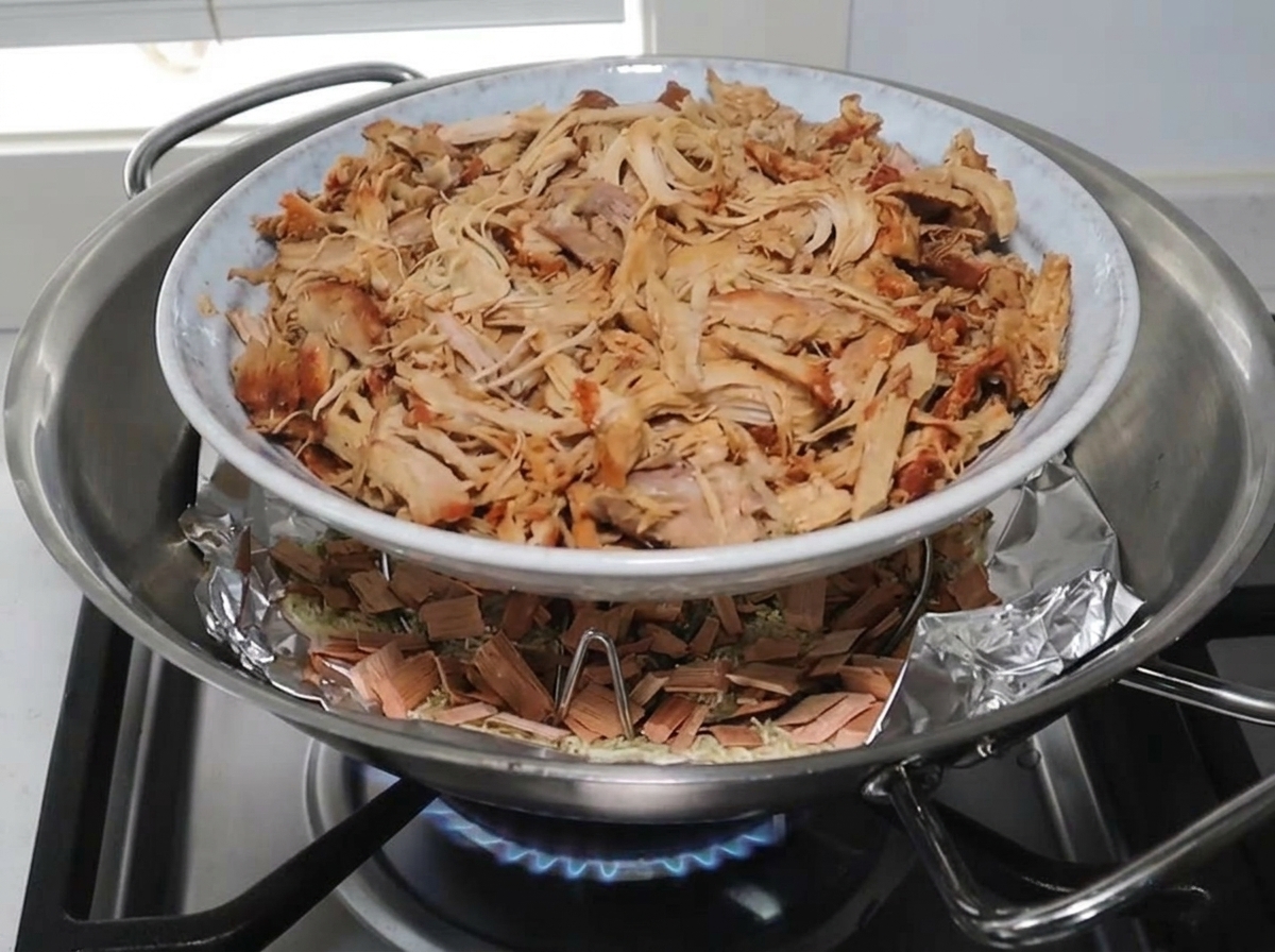 Un plato de cerdo desmenuzado sobre una rejilla dentro del wok sobre la mezcla de ahumado.