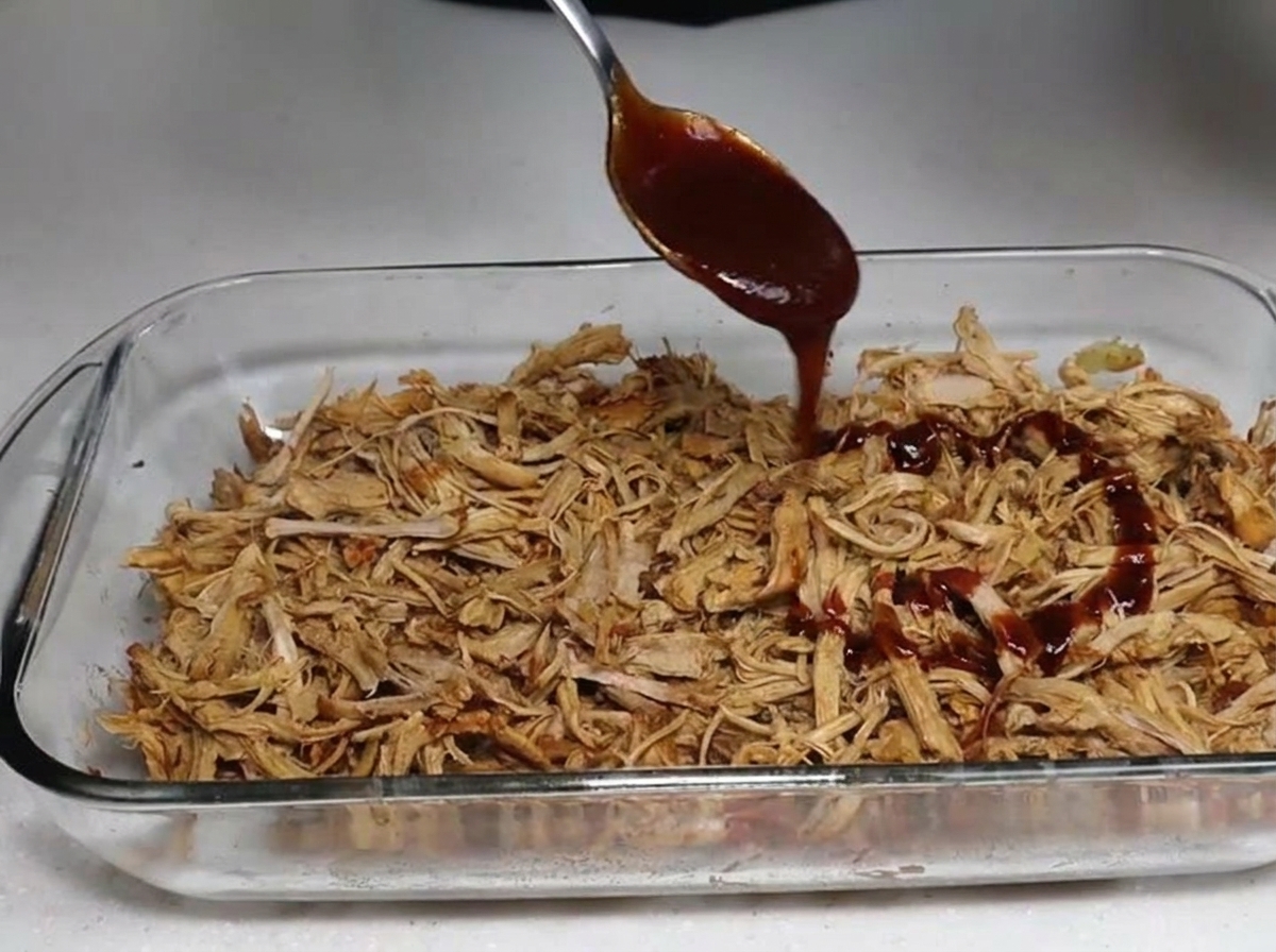 Salsa BBQ siendo servida con cuchara sobre cerdo desmenuzado.