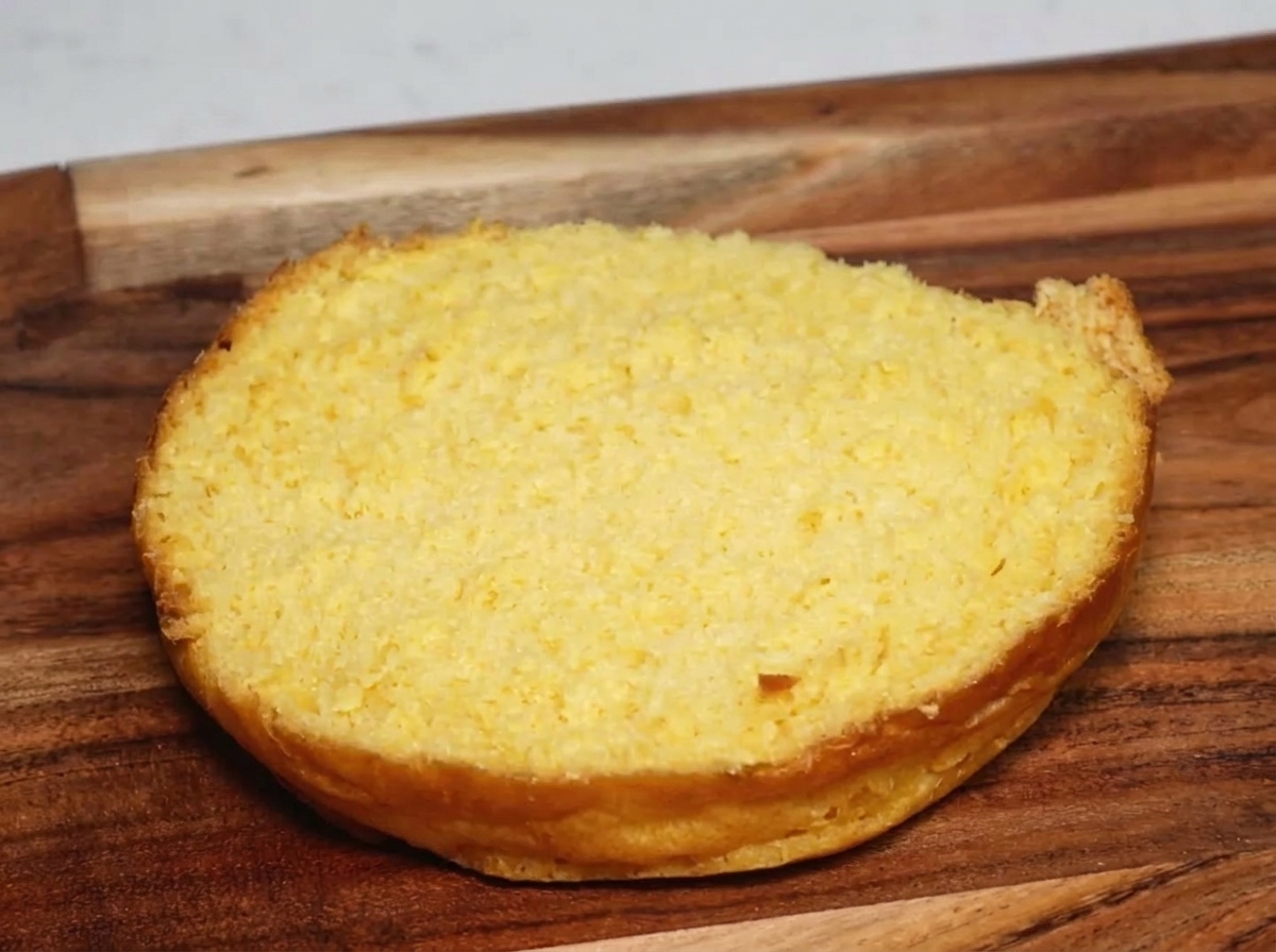 Un pan de hamburguesa tostado recibiendo una porción de cerdo desmenuzado con salsa.