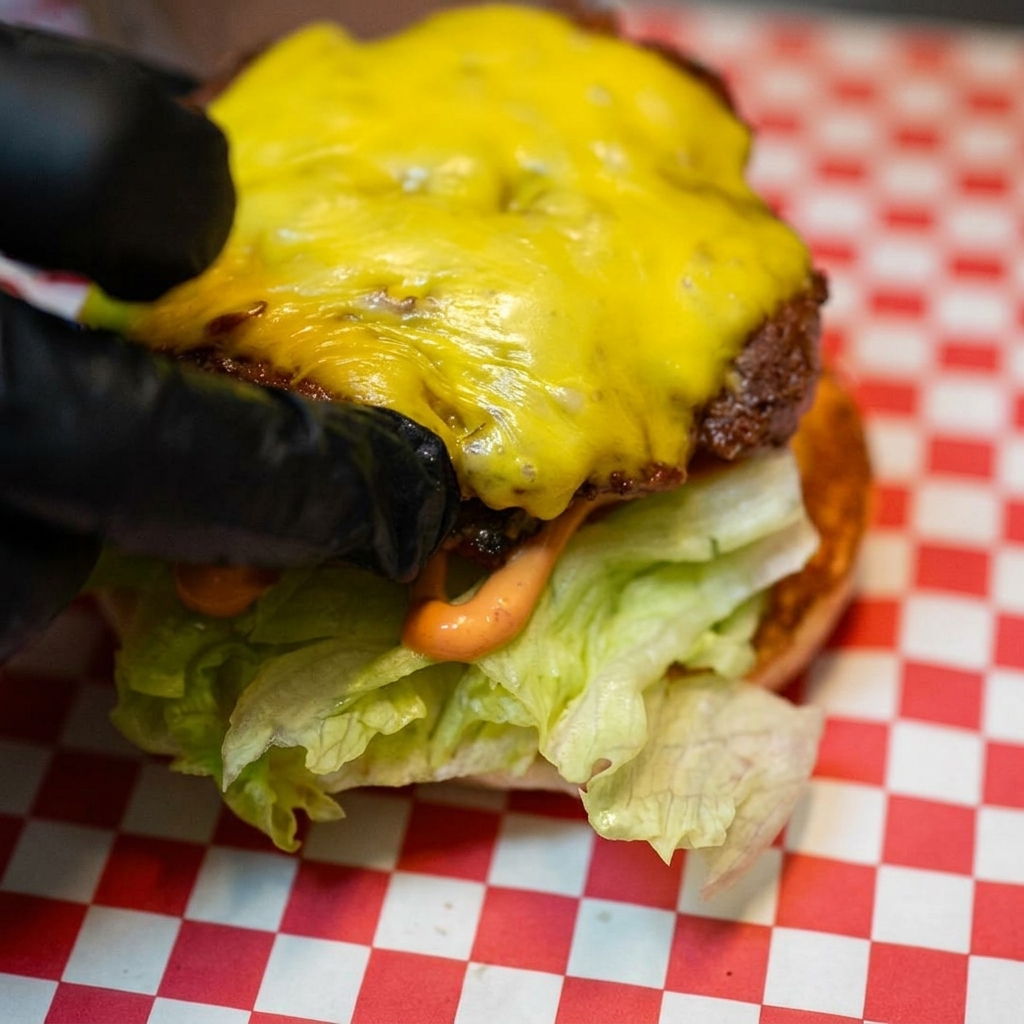 La hamburguesa cubierta de queso siendo colocada sobre la base de lechuga y tomate.