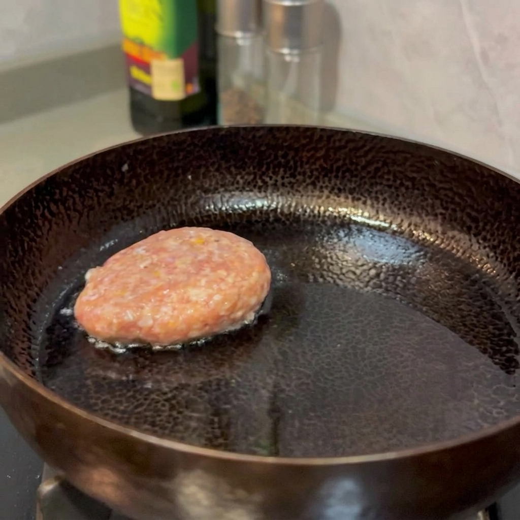 Hamburguesas de ternera friéndose en una sartén hasta quedar doradas y firmes.