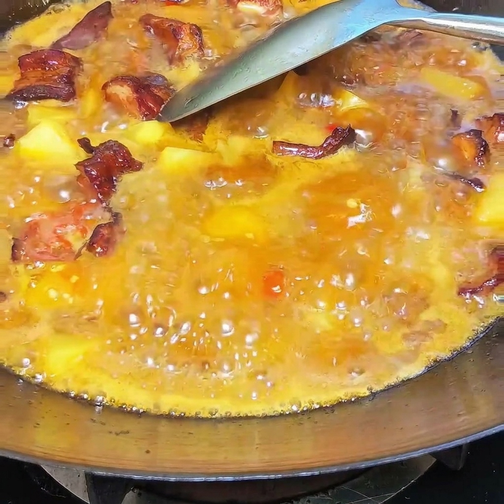 Una cucharada de manteca blanca cremosa mezclándose en el guiso burbujeante de costillas y patatas en un wok.
