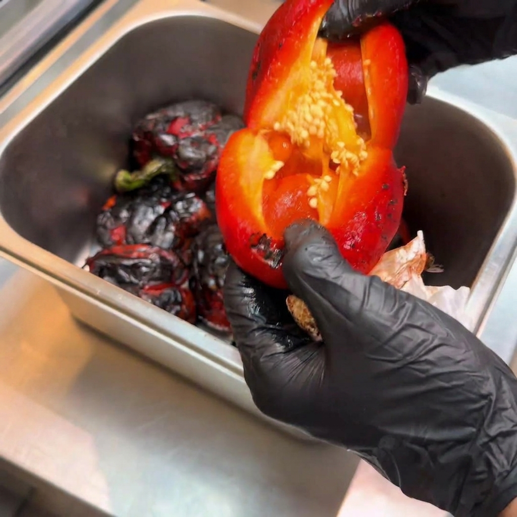 Pimiento rojo asado abierto revelando el interior con las semillas siendo retiradas.