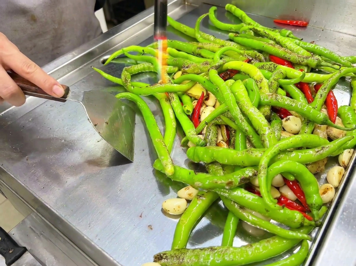 La llama de un soplete carbonizando el exterior de los chiles sobre la plancha.