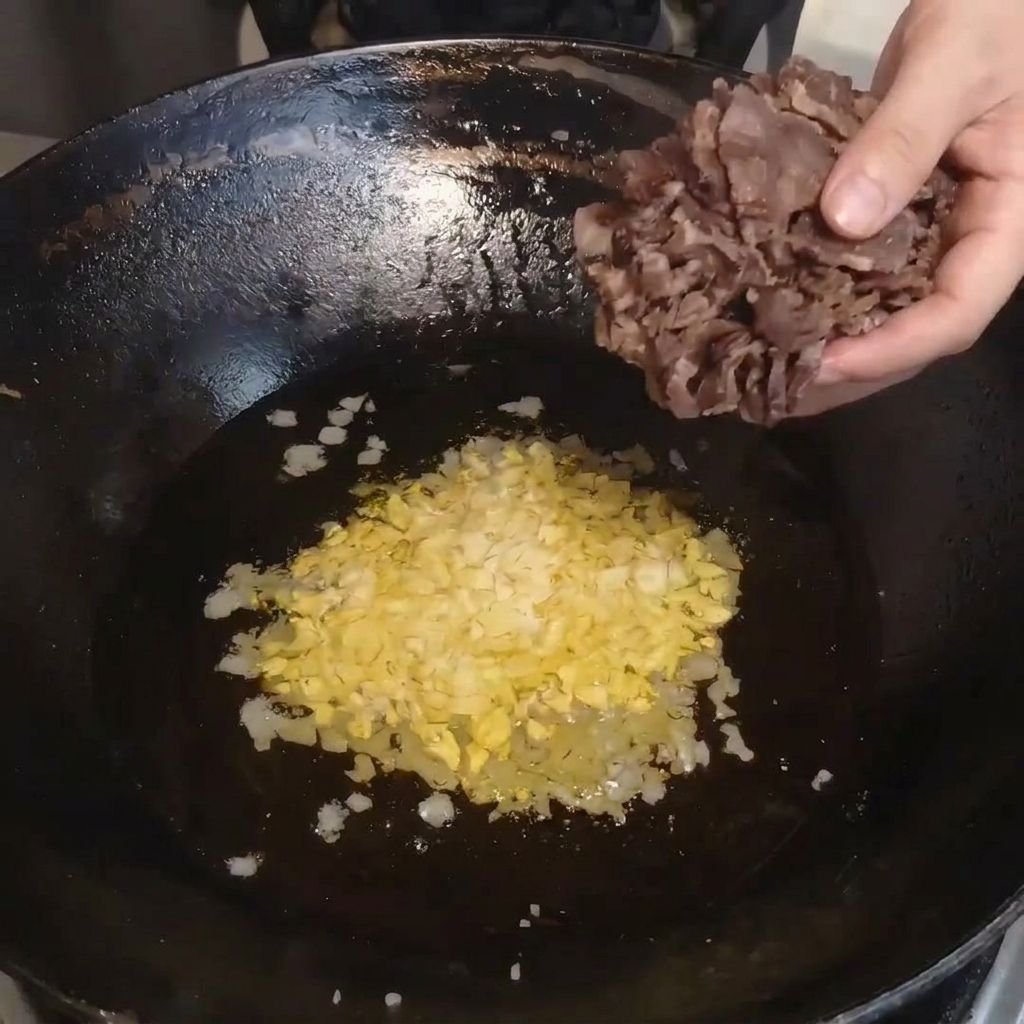 Rodajas de carne curada al vapor siendo transferidas de un bol a un wok caliente.