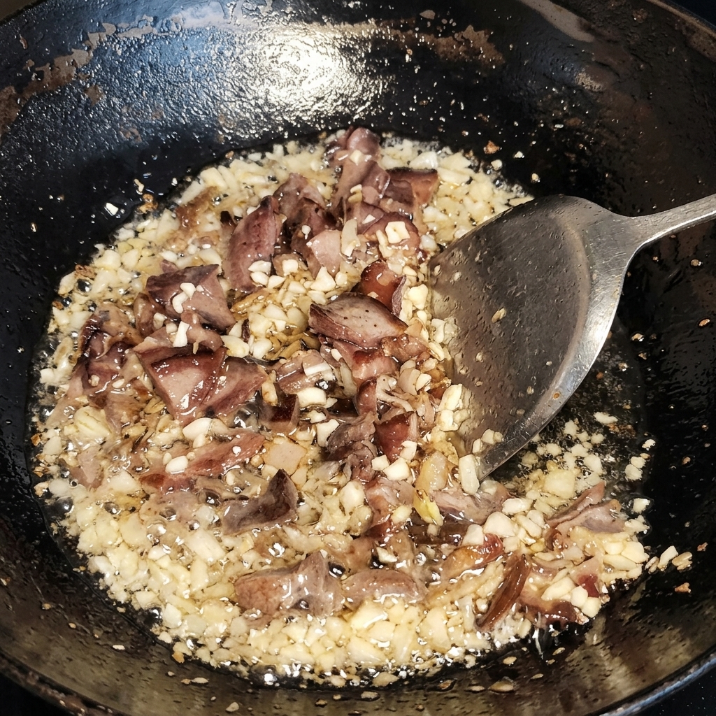 Carne y ajo salteándose en un wok con una espátula, con el aceite burbujeando claramente alrededor de los ingredientes.