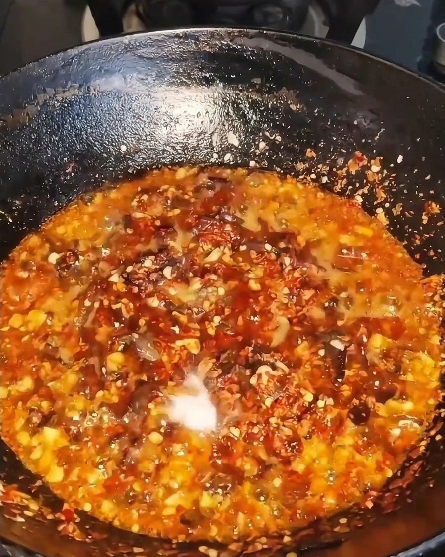 Condimento líquido oscuro vertiéndose en un wok humeante lleno de carne, chile y aromáticos.