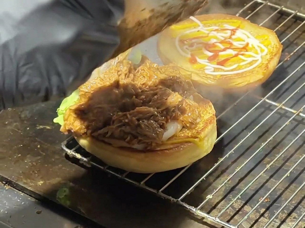Cerdo desmenuzado con salsa siendo servido sobre un pan tostado con lechuga en una plancha.