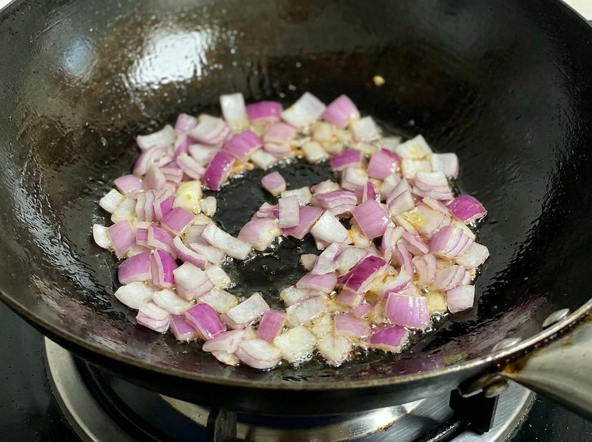 Cebolla roja picada friéndose en un wok caliente con aceite, siendo removida por una espátula negra.