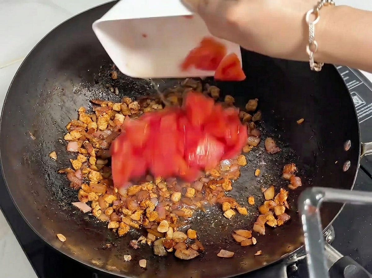 Tomates rojos frescos recién cortados siendo añadidos desde un cuenco blanco en un wok que contiene carne picada cocinada.