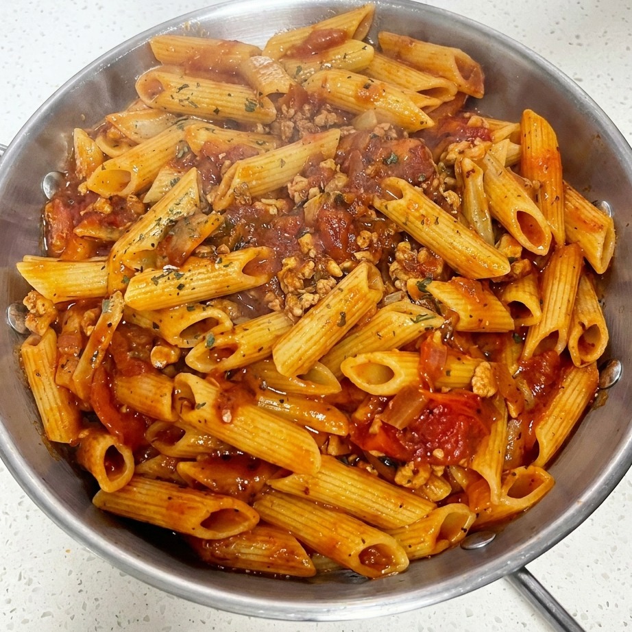 Un primer plano de una sartén de macarrones con salsa de carne y tomate cubiertos con una loncha de queso y hierbas verdes secas espolvoreadas.