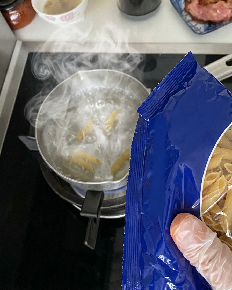 Pasta penne seca siendo vertida desde un paquete en una olla con agua hirviendo.
